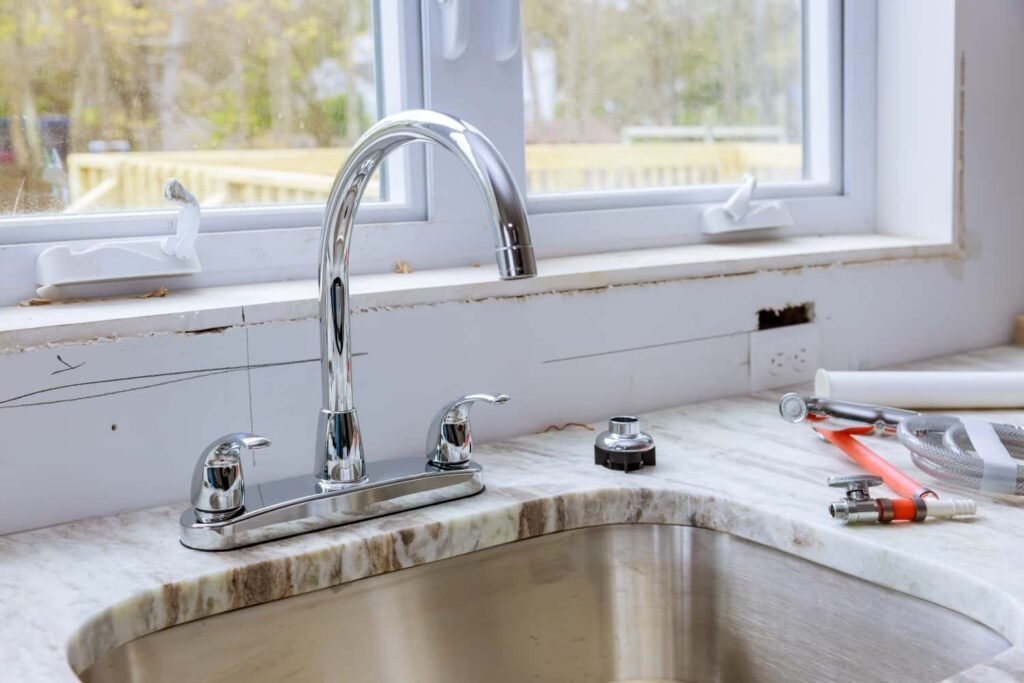 Chrome faucet installation in a kitchen setting with a sink, showcasing plumbing fixtures and tools, relevant to plumbing services and home repairs.